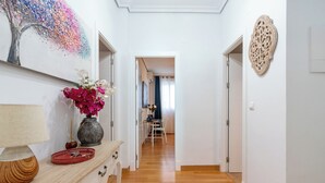 A hallway with a wooden floor, a desk with a lamp and a vase of flowers, and a painting on the wall. - Jesús Gran Poder A. 2 bedrooms (Sevilla)
