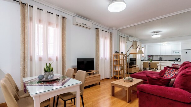 A modern living room with a glass dining table, a red sofa, and a TV. - Jesús Gran Poder A. 2 bedrooms (Sevilla)