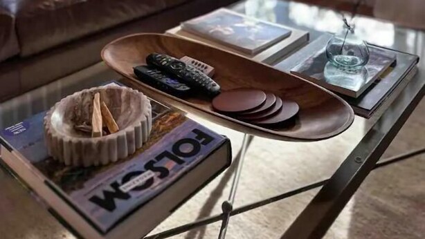 A living room with a leather sofa, a glass coffee table with remote controls, a bowl, and a magazine.