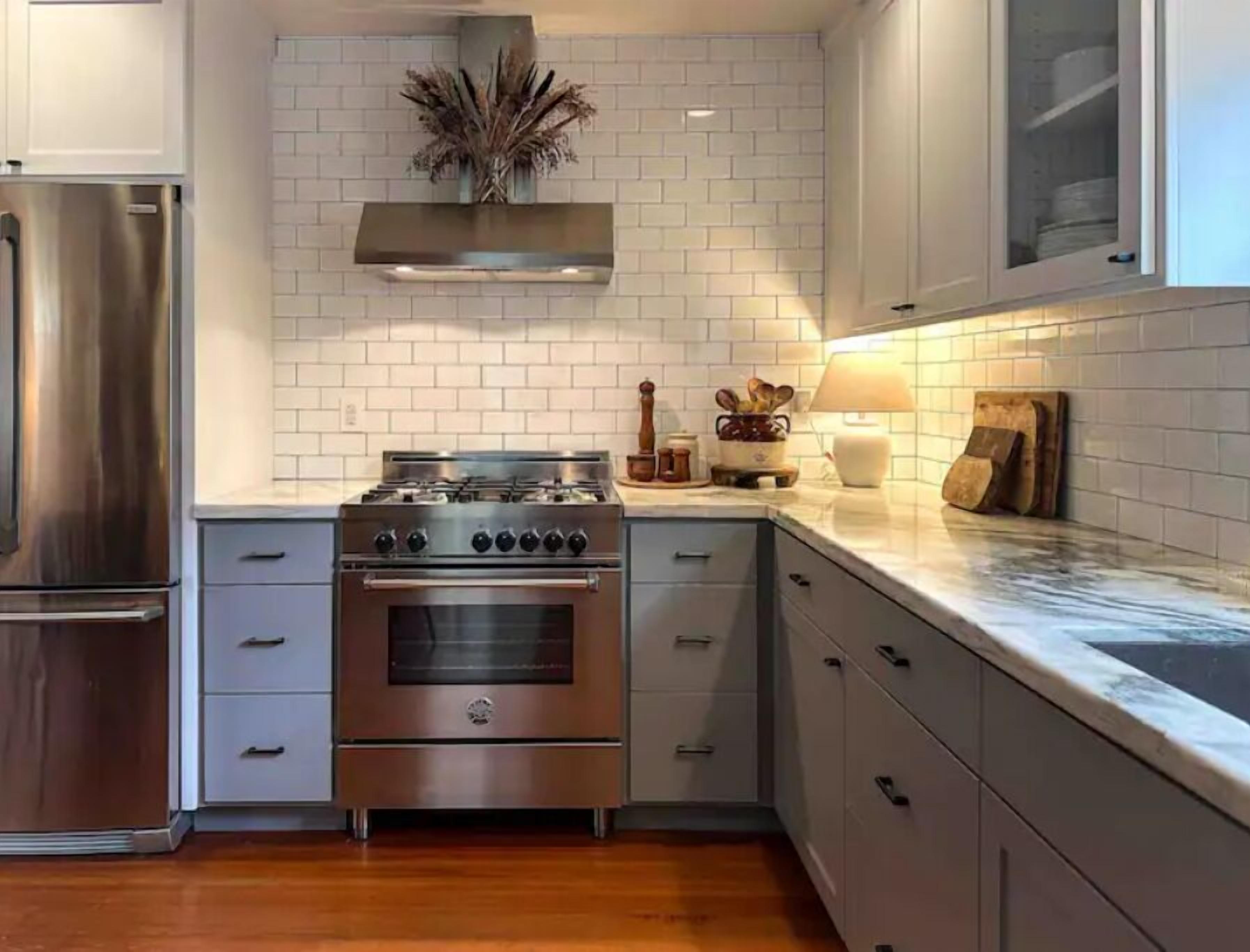 A modern kitchen with a stainless steel stove, oven, and refrigerator, light gray cabinets, and a white tiled backsplash.