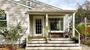 A house with a stone-paved front porch, a white door, and a window with a view of the backyard.