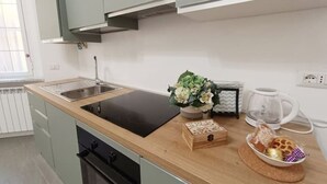 A modern kitchen with a wooden countertop, a black cutting board, a vase with flowers, a coffee maker, and a bowl of bread. - Welcome Studio 36, 15 minutes to Duomo (Milano)