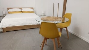 A bedroom with a bed, a round glass table, two yellow chairs, and a small side table with a lamp. - Welcome Studio 36, 15 minutes to Duomo (Milano)
