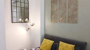A room with a sofa, two yellow cushions, a mirror, and a wall decoration. - Welcome Studio 36, 15 minutes to Duomo (Milano)