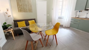 A modern living room with a glass-top dining table, two yellow chairs, a grey chair, and a grey sofa with yellow cushions. - Welcome Studio 36, 15 minutes to Duomo (Milano)