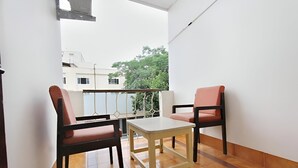 A balcony with two chairs and a small table, white walls, and a view of buildings and trees. - Hotel Telehaus Lalbagh Botanical Garden (Bengaluru)