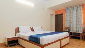 A bedroom with a bed, bedside table, and a small desk with a chair. - Hotel Telehaus Lalbagh Botanical Garden (Bengaluru)