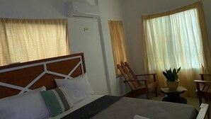 Habitación de hotel con cama, una silla, una mesita y una planta en maceta.