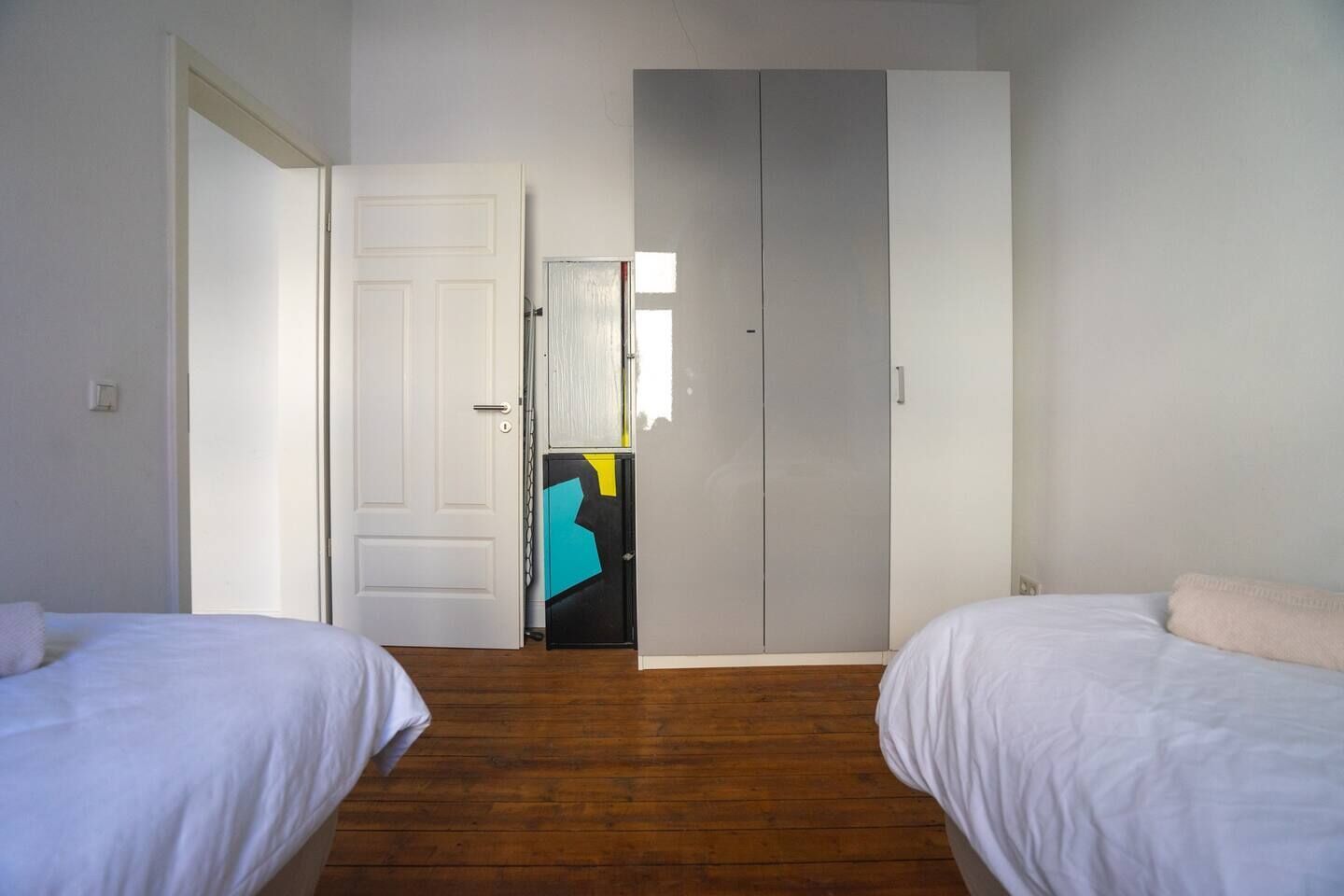 Ein Zimmer mit zwei Betten, einem Kleiderschrank und einer Tür zu einem anderen Raum.