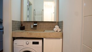Un baño pequeño con lavadora, lavamanos y espejo.