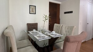 Zona pranzo con tavolo in vetro, quattro sedie e un vaso con una pianta.