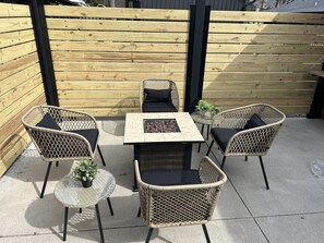 Un espace extérieur aménagé en terrasse, avec des meubles en osier, notamment des chaises et une table, ainsi qu’un petit foyer.