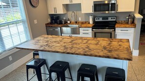 A kitchen with white cabinets, a stainless steel microwave, a stove, and a wooden countertop. There are three black stools and a window with blinds. -  The "Stable" at OGR!  5 Star Accommodations! 
Resort pool and spa!  Sleeps 4 (Holland)
