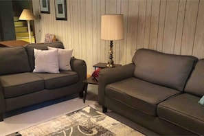 A living room with two dark sofas, a small table, a lamp, and a patterned rug. - Country Crossroads (Armstrong Creek)