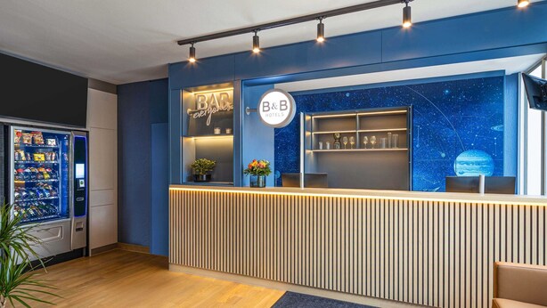 Una reception di un hotel con una parete blu, un cartello B&B, una macchina distributrice e un pavimento in legno.