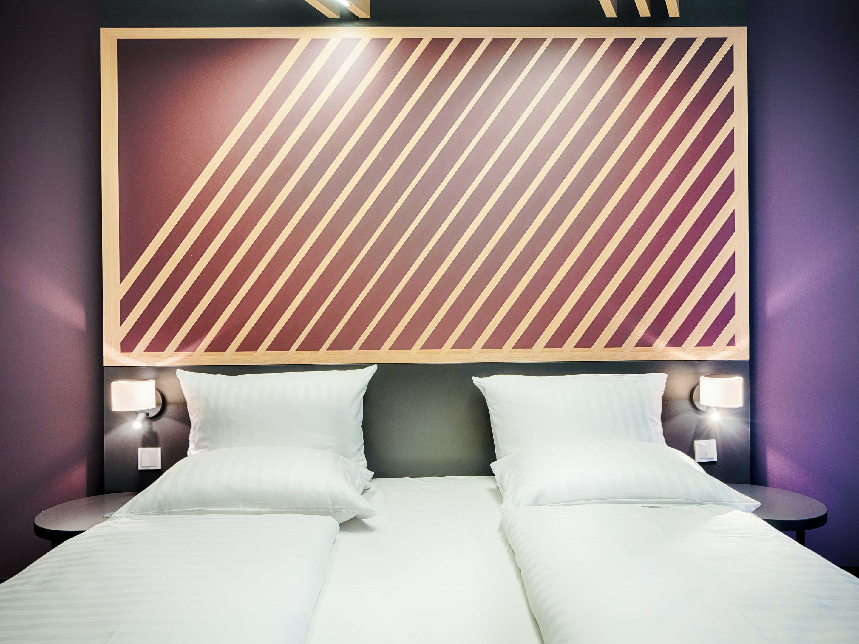 A hotel room with a large bed, two bedside tables with lamps, and a patterned wall above the bed.