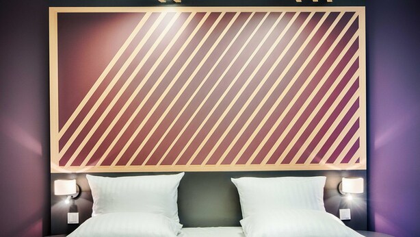 Une chambre d’hôtel avec un grand lit, deux tables de chevet avec des lampes et un mur décoré d’un motif au-dessus du lit.