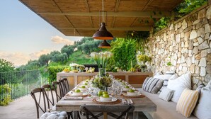 Un espace extérieur aménagé pour les repas, avec un mur en pierre, une table en bois et des chaises.