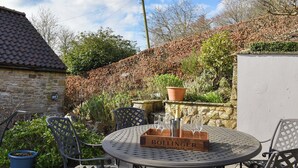 A round metal table with four chairs, a bottle of champagne, and a box labeled "Bollinger" in a garden setting. - 2 bedroom accommodation in Helmsley (Helmsley)