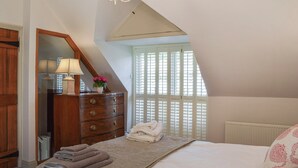 A bedroom with a bed, a dresser, a mirror, a chandelier, and a window with shutters. - 2 bedroom accommodation in Helmsley (Helmsley)
