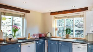 A kitchen with blue cabinets, a dishwasher, a red toaster, and a window with a view of greenery. - 2 bedroom accommodation in Helmsley (Helmsley)