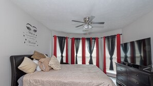 Een slaapkamer met een bed, een plafondventilator, een dressoir en een televisie.