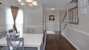 Een eethoek met een witte tafel en stoelen, een kroonluchter en een trap met een houten leuning.