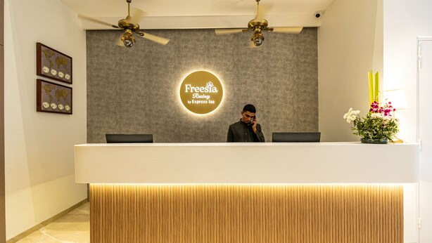 A reception desk with a modern design, featuring a logo in the center, two ceiling fans, and a world map decoration on the wall. - Freesia Residency By Express Inn - Navi Mumbai (Navi Mumbai)