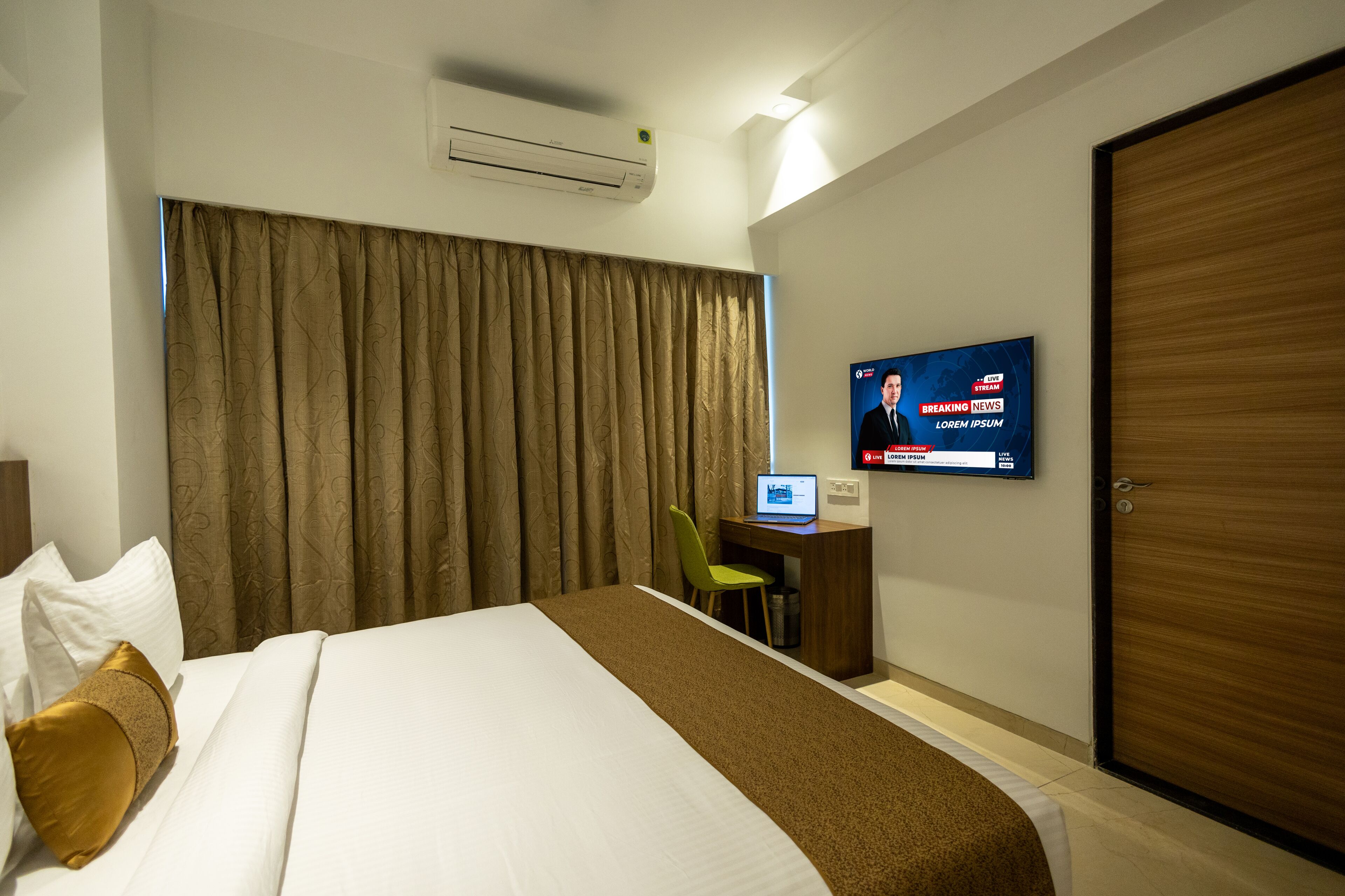 Habitación de hotel con cama, escritorio con computadora, televisor mostrando noticias y armario.