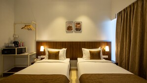 A hotel room with two beds, a wooden headboard, bedside lamps, a coat rack, and a small desk with a telephone and a coffee maker. - Freesia Residency By Express Inn - Navi Mumbai (Navi Mumbai)