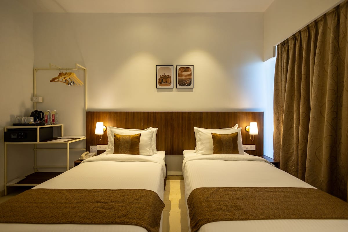 A hotel room with two beds, a wooden headboard, bedside lamps, a coat rack, and a small desk with a telephone and a coffee maker.