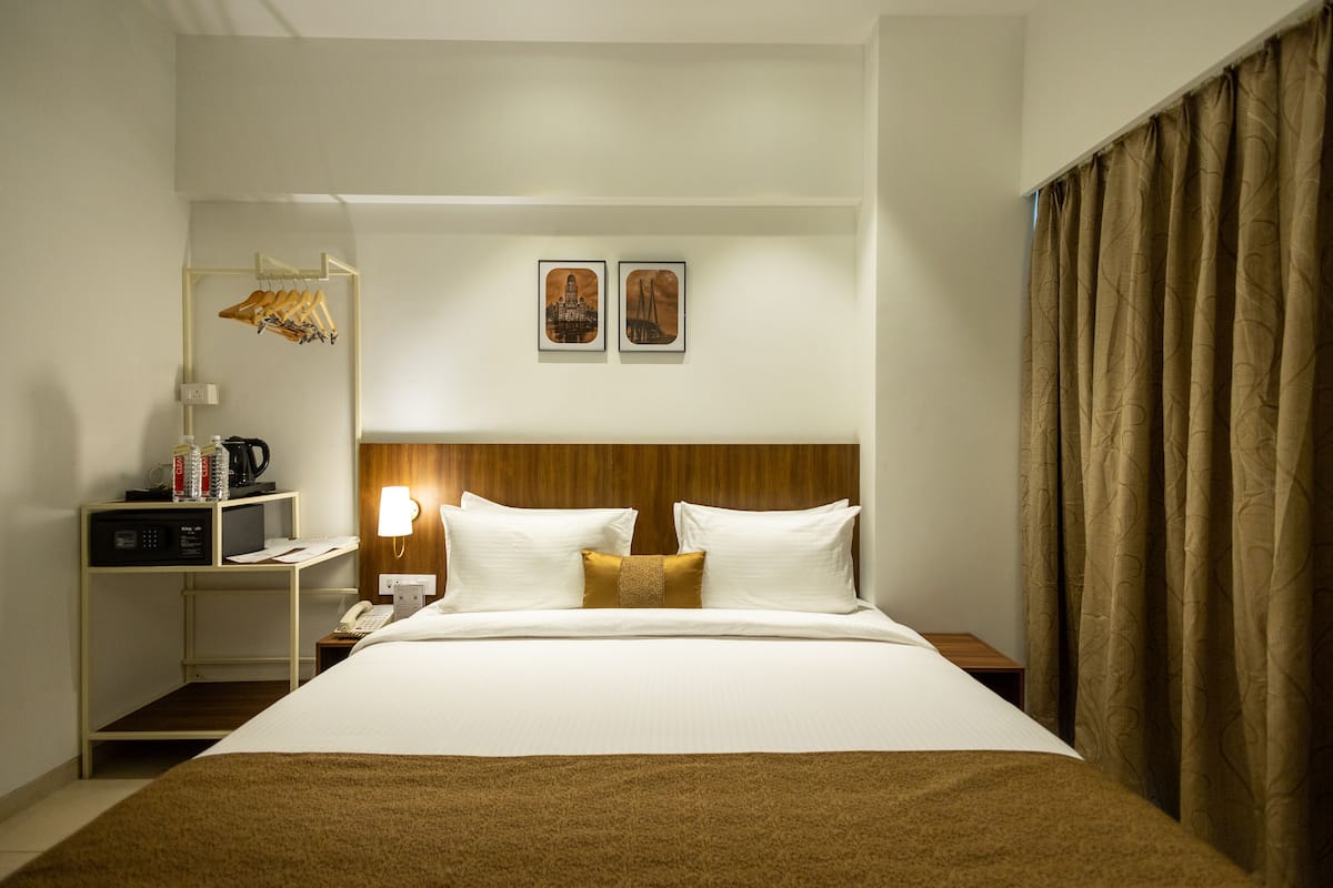 A hotel room with a large bed, a bedside table with a lamp, a small desk with a telephone, and a coat rack.