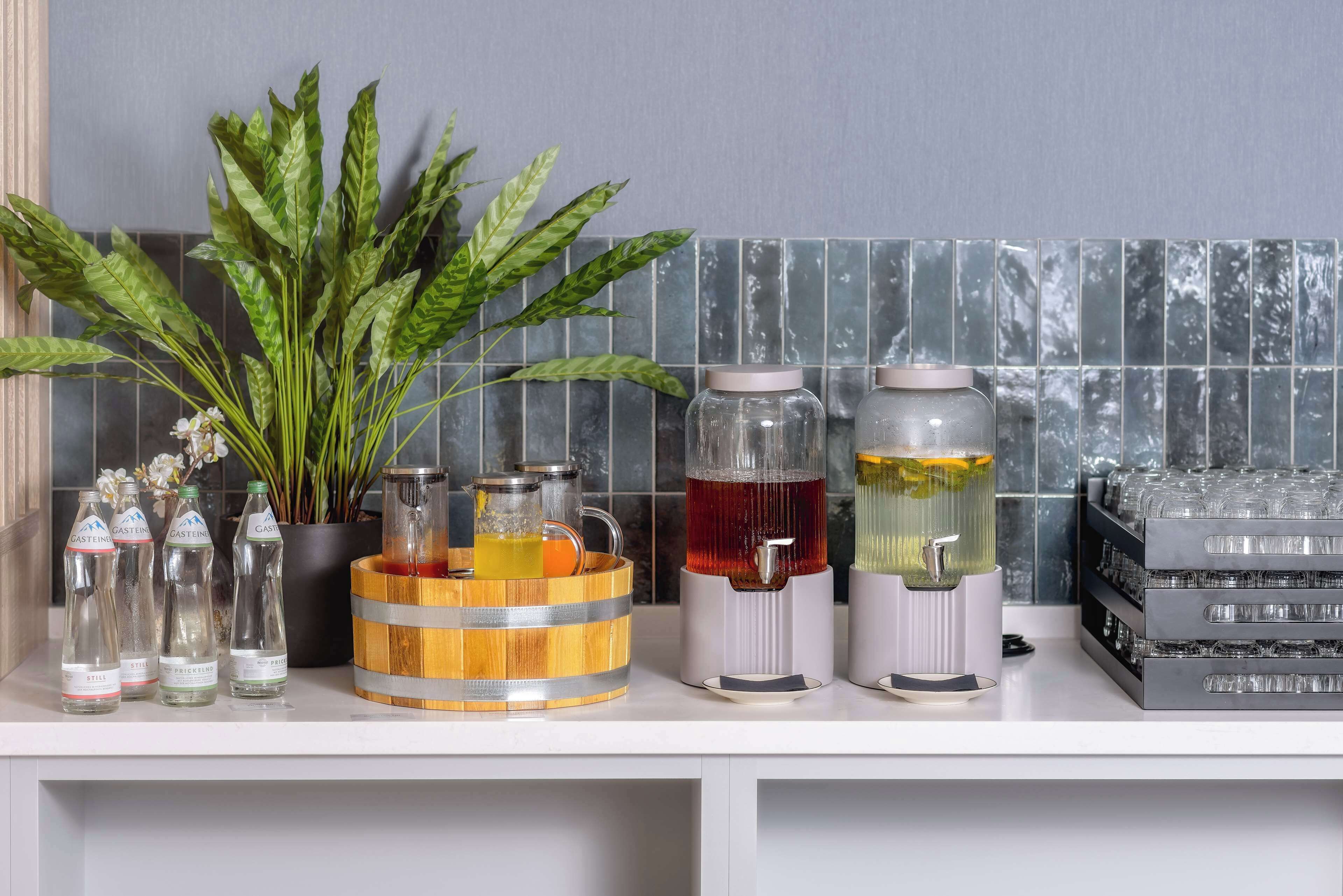 A kitchen counter with various drink dispensers, a potted plant, and a wooden barrel.