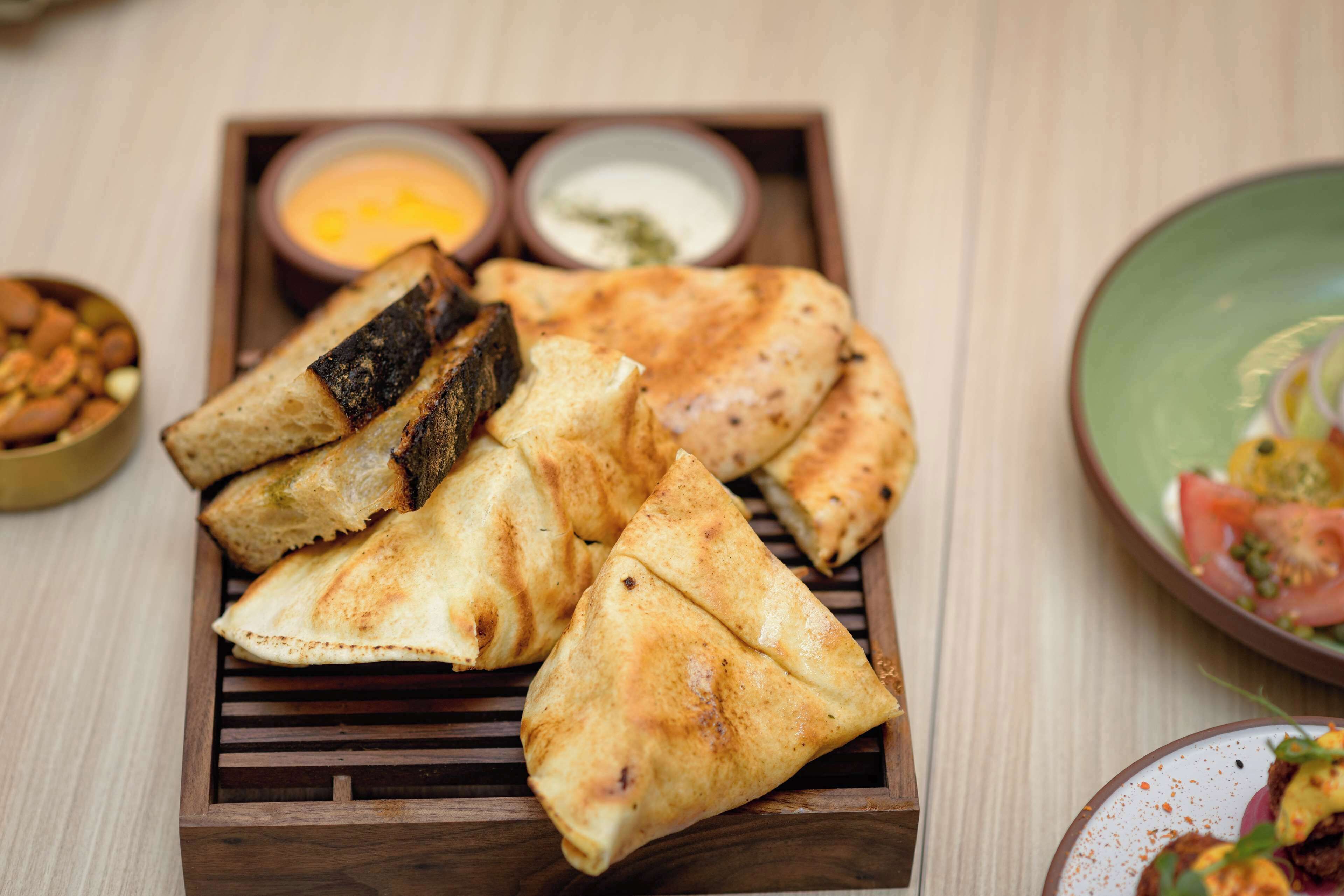 A tray of samosas with dipping sauces and a bowl of nuts.