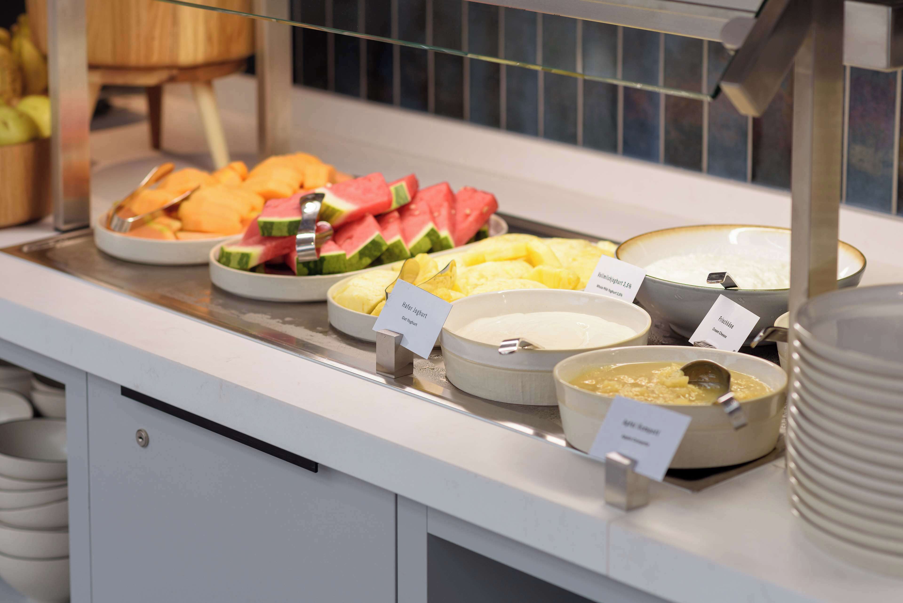 A buffet counter with various food items including fruits and dishes labeled with names.