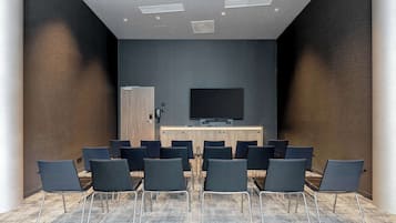 A conference room with a large flat-screen TV, rows of chairs, and a wooden panel wall.