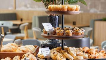 Una exhibición escalonada de productos de repostería que incluye muffins, croissants y pan, con etiquetas que identifican los tipos de comida disponibles.