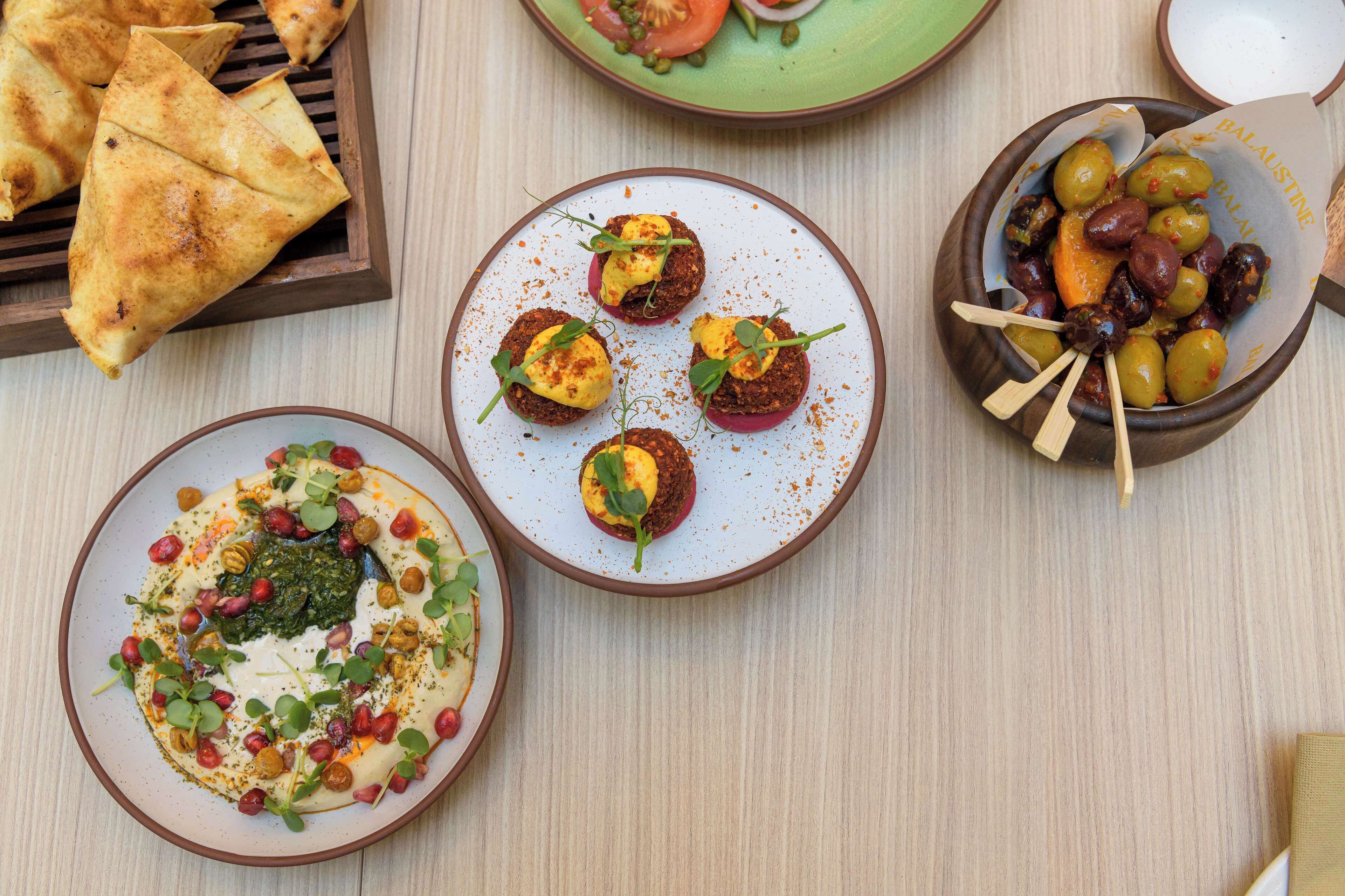 Variedad de platos en una mesa, incluyendo un plato con ensalada verde, un plato con salsa roja y un plato con aceitunas y un pincho.