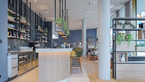 A modern bar area with a curved counter, shelves with bottles, and hanging plants. - Radisson Hotel Graz (Graz)
