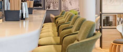 A row of green upholstered chairs with a modern bar area in the foreground.