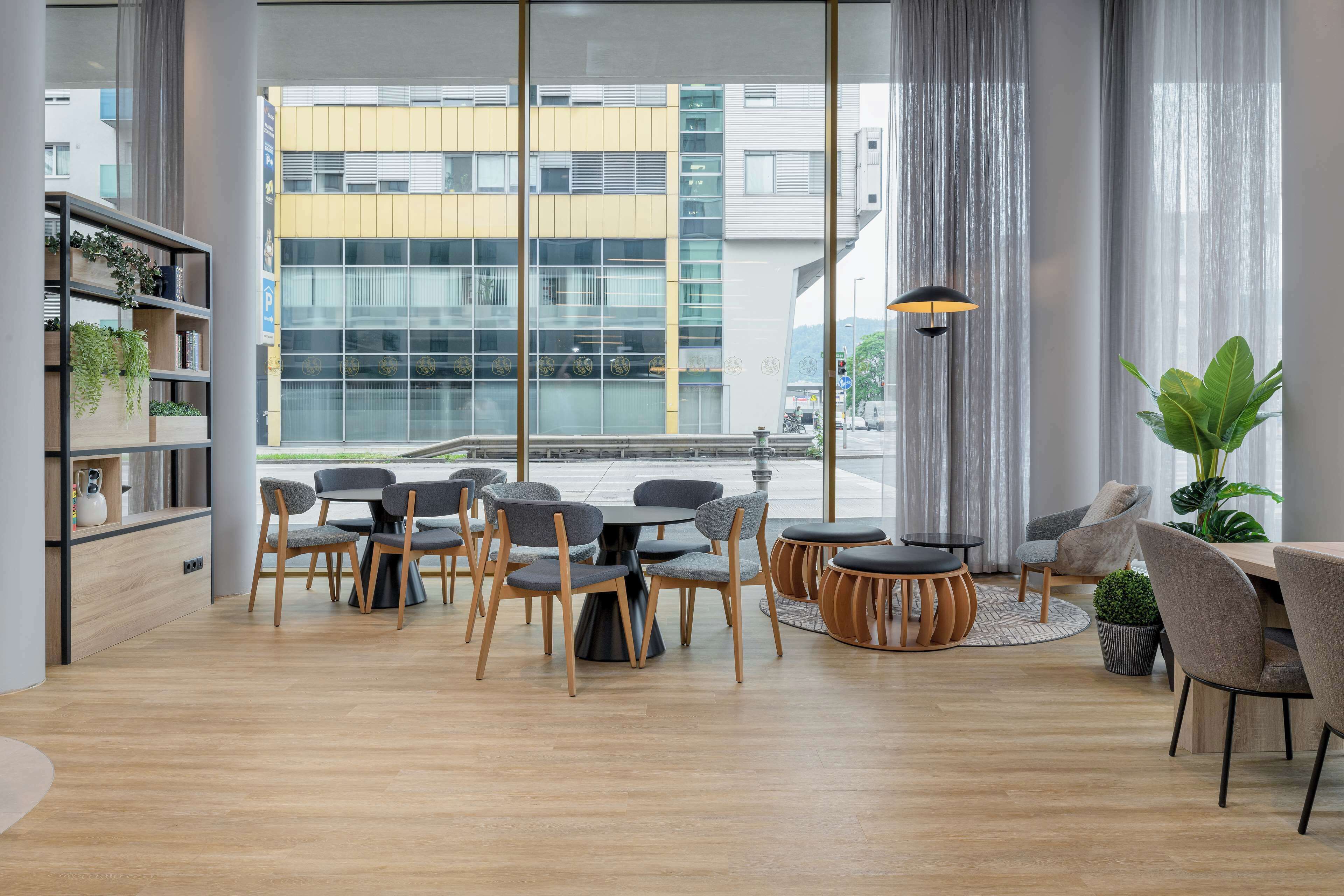 Interior moderno com área de refeições, uma estante com plantas e grandes janelas com vista para a cidade.