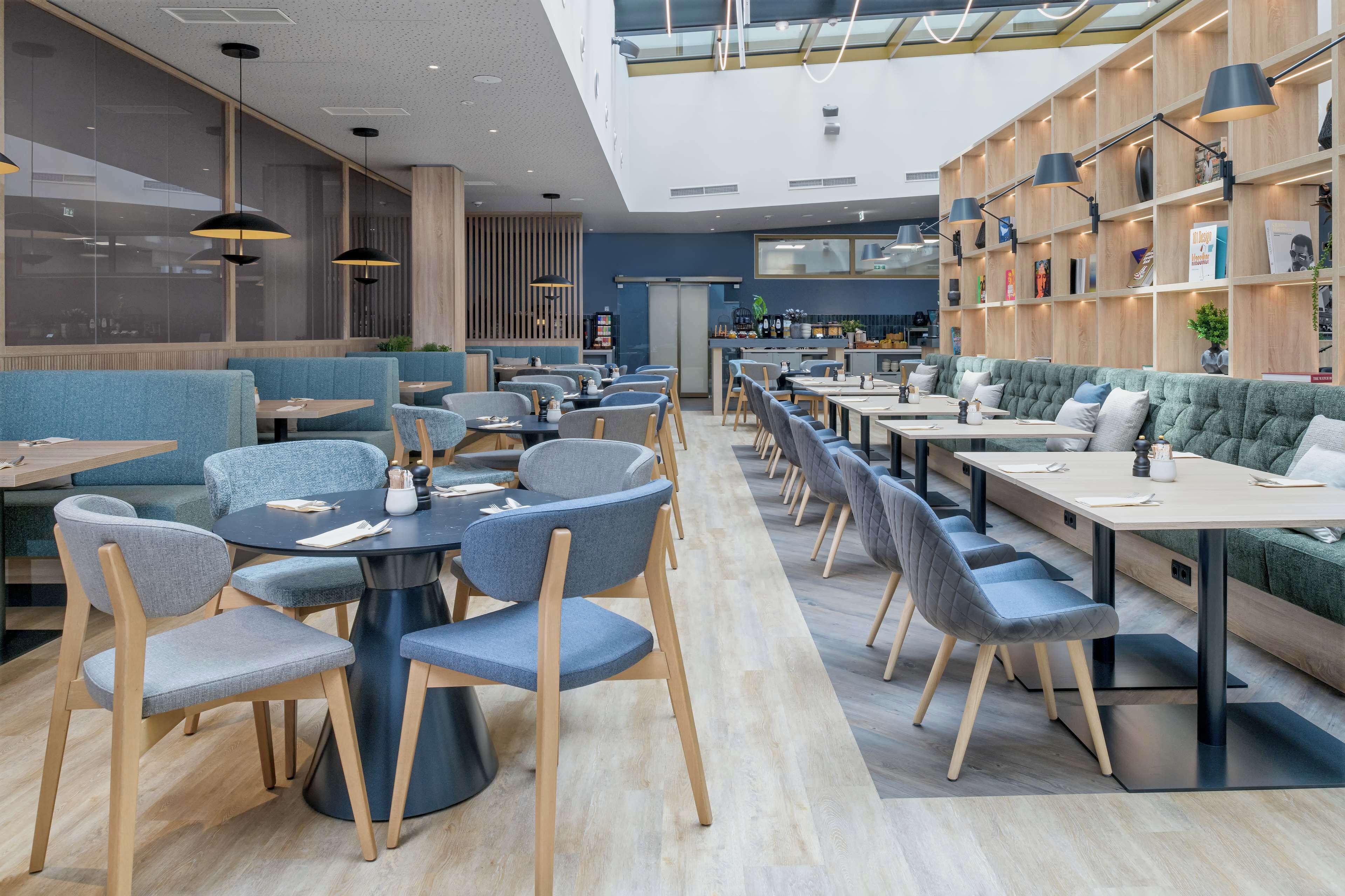 A modern restaurant with high ceilings, wooden bookshelves, and a variety of seating options including tables and booths.