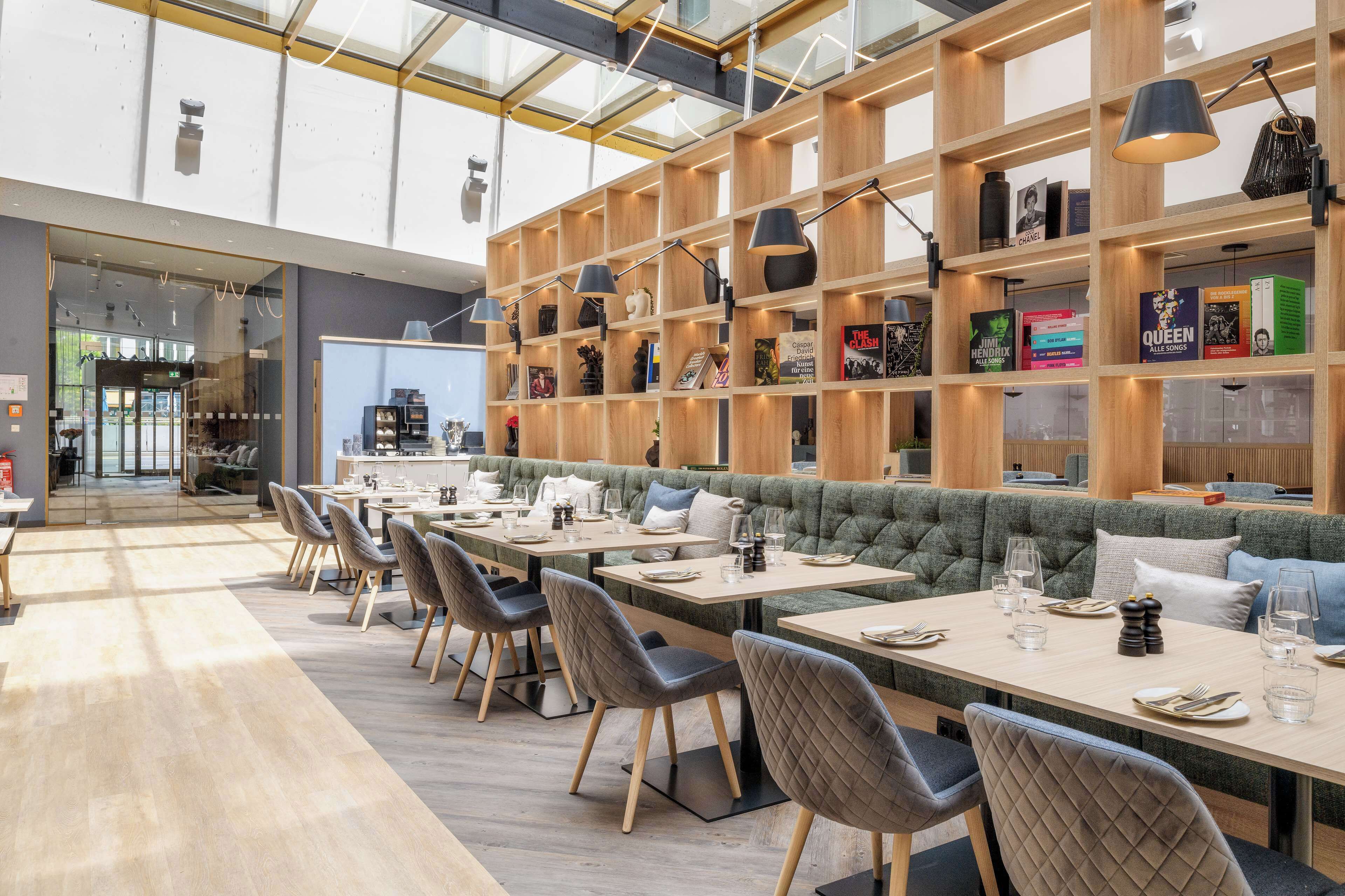 A modern restaurant with wooden shelves, tables, and a green cushioned seating area.