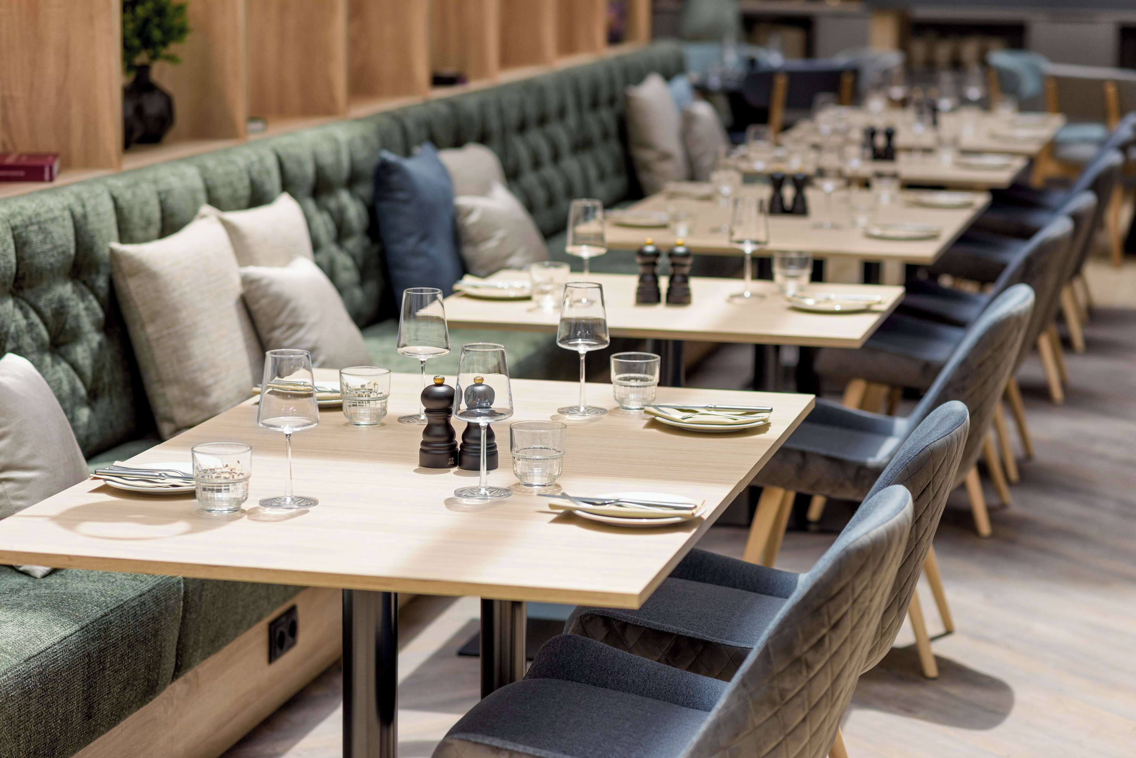 A restaurant with a long, cushioned bench seating area and individual tables with set dining ware.