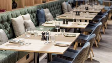 A restaurant with a long, cushioned bench seating area and individual tables with set dining ware.