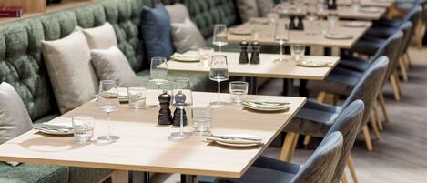 A restaurant with a long, cushioned bench seating area and individual tables with set dining ware.