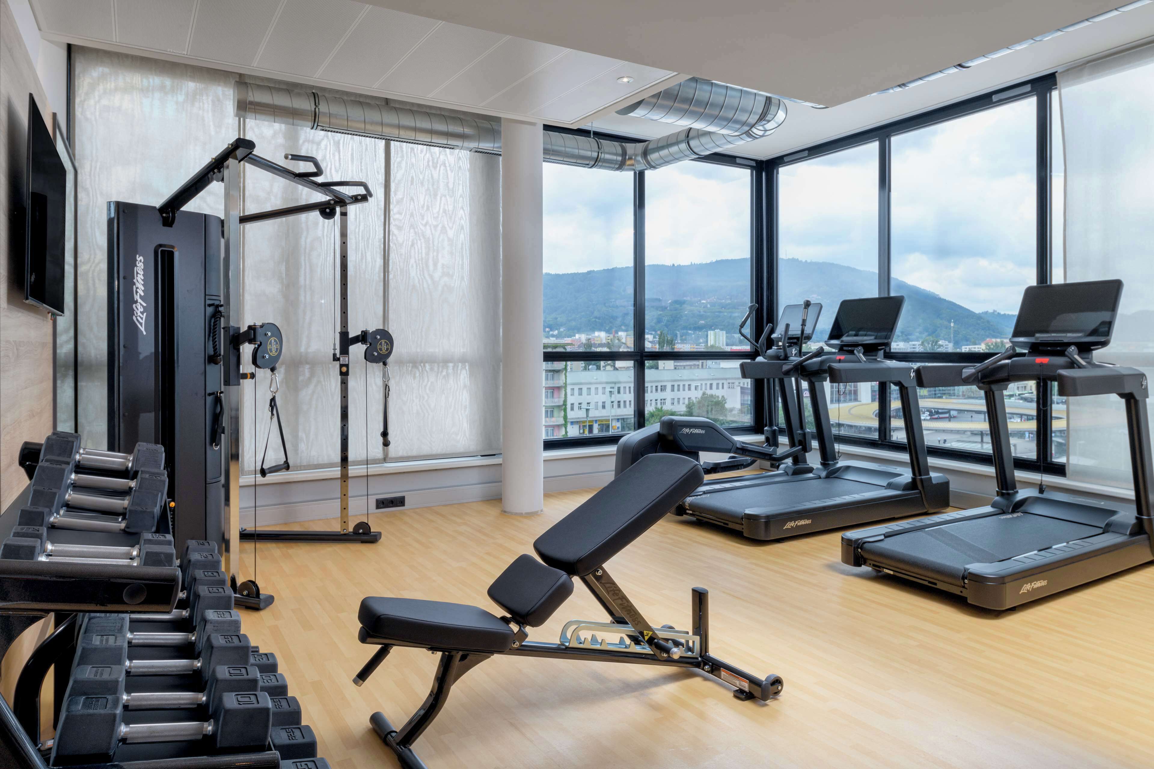 A modern gym with cardio equipment, weight machines, and a bench.