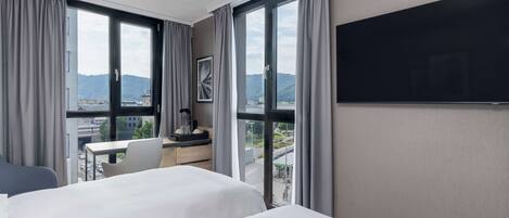 A hotel room with two beds, a desk, and a TV.