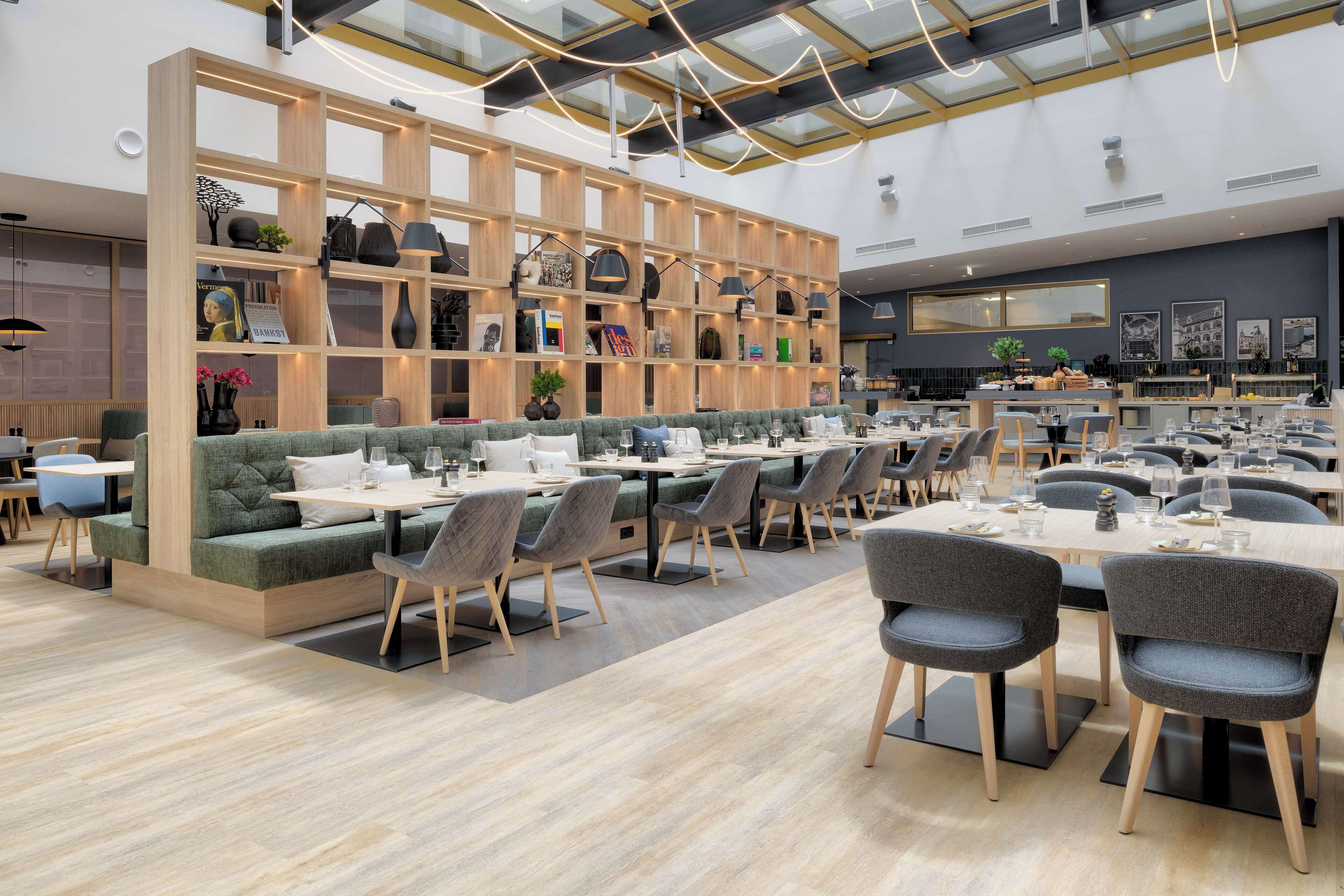 Un restaurante moderno con estantes de madera, asientos acolchados y diferentes opciones de mesas.