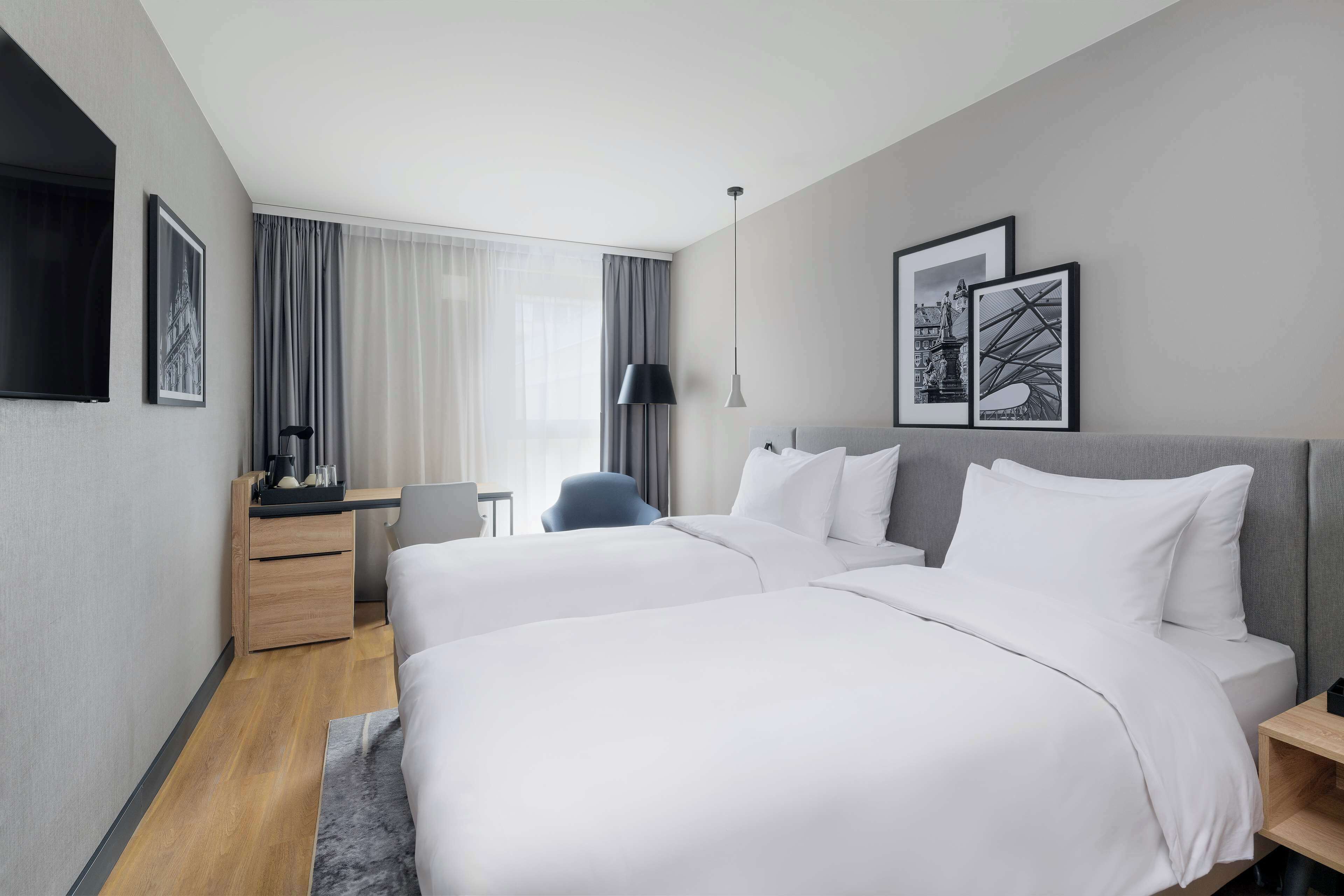 Habitación de hotel con dos camas, un escritorio, una silla y obras de arte en las paredes.
